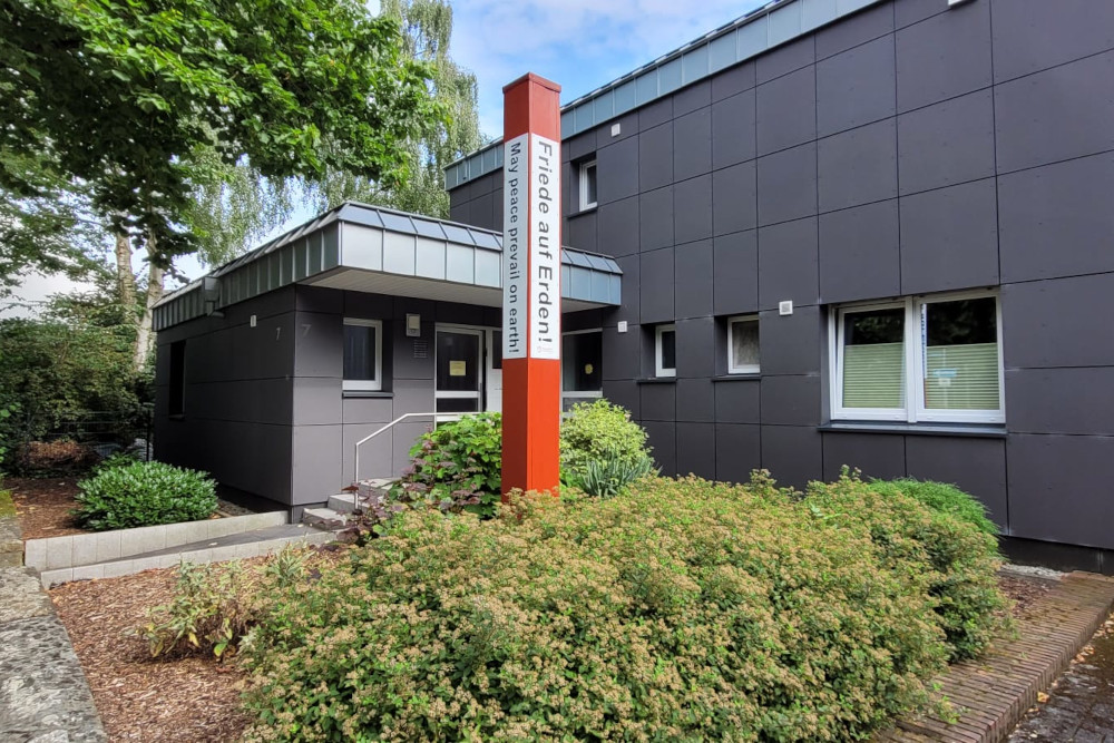 Bild vom Pfarrhaus. Davor steht ein Friedensmahner.