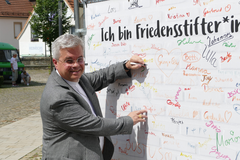 Erzbischof Dr. Udo Markus Bentz unterschreibt das Plakat. Ich bin Friedensstifter.