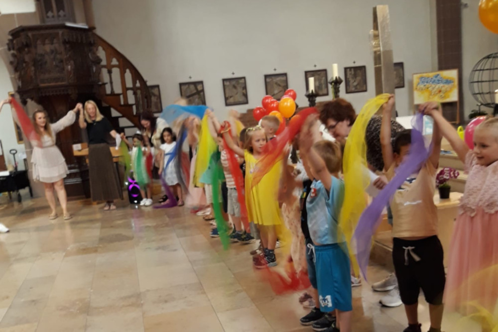 Gruppe von Kindern und Erziehern winken mit bunten Tüchern
